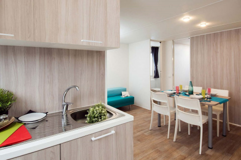 Moderne glamping-accommodatie met keuken, eettafel voor vier personen en een blauwe bank in de zithoek.