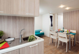 Moderne glamping-accommodatie met keuken, eettafel voor vier personen en een blauwe bank in de zithoek.