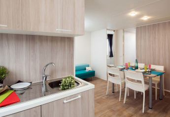 Modern glamping accommodation featuring a kitchen area, dining table for four, and a blue sofa in the lounge.