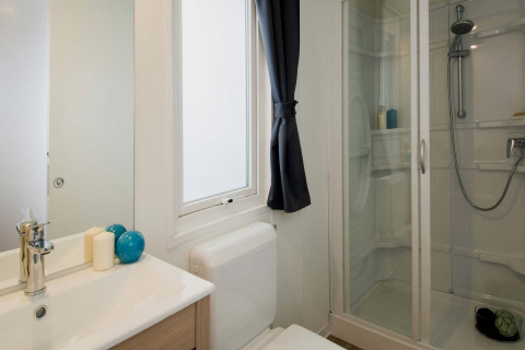 Moderne badkamer in een glampingaccommodatie met douchecabine, raam, wastafel en decoraties.
