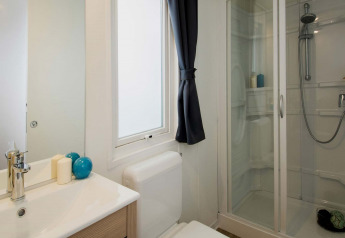 Salle de bain moderne dans un hébergement glamping avec douche, fenêtre, lavabo et objets décoratifs.