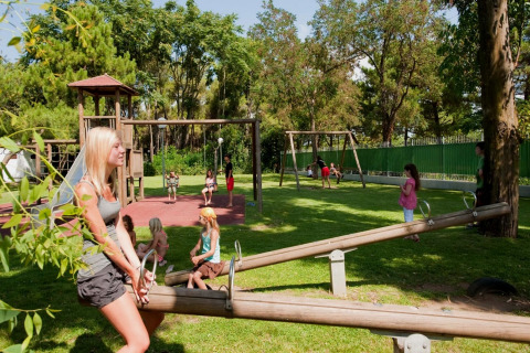 Kinderen en volwassenen spelen op een glamping speeltuin met schommels, glijbaan en grasveld.