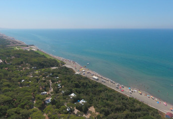 Vue aérienne d’un site de glamping près de la plage, avec végétation, parasols et mer bleu clair.