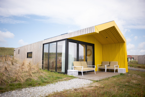 Buitenaanzicht van Resort Callantsoog 2 met gele veranda, grote ramen en moderne tuinmeubelen.