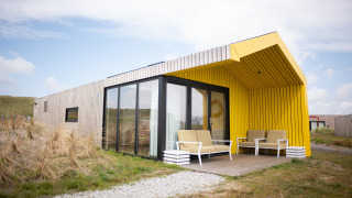 Außenaufnahme der Resort Callantsoog 2-Lodge mit gelber Veranda, großen Fenstern und modernen Möbeln.