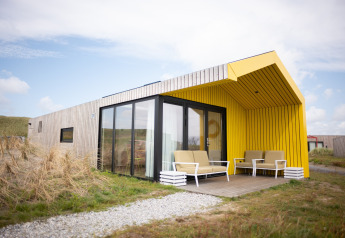 Udendørs foto af Resort Callantsoog 2-lodge med gul overdækket terrasse, store vinduer og moderne design.