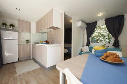 Moderne Mobilheim-Küche und Essbereich mit Holzmöbeln, Croissants und Blick ins Schlafzimmer in Italien.