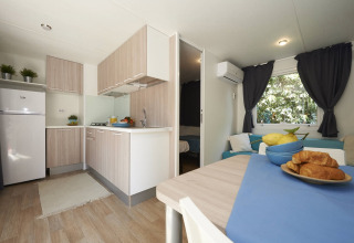 Moderne Mobilheim-Küche und Essbereich mit Holzmöbeln, Croissants und Blick ins Schlafzimmer in Italien.