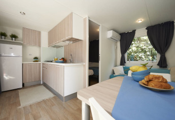Moderne Mobilheim-Küche und Essbereich mit Holzmöbeln, Croissants und Blick ins Schlafzimmer in Italien.
