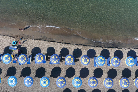 Luftaufnahme vom Strand bei Baia Domizia Villaggio Camping I4 in Italien mit bunten Sonnenschirmen und Liegen.
