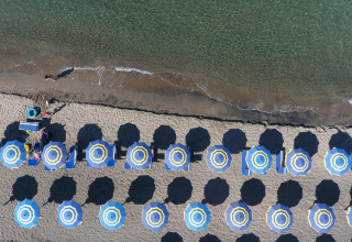 Luftaufnahme vom Strand bei Baia Domizia Villaggio Camping I4 in Italien mit bunten Sonnenschirmen und Liegen.