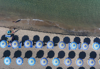 Luftaufnahme vom Strand bei Baia Domizia Villaggio Camping I4 in Italien mit bunten Sonnenschirmen und Liegen.