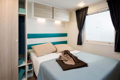 Slaapkamer in Baia Domizia Villaggio Camping I2 stacaravan, tweepersoonsbed en groot raam, modern interieur.