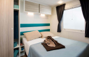 Bedroom inside Baia Domizia Villaggio Camping I2 mobile home, double bed, minimalist decor, large window.