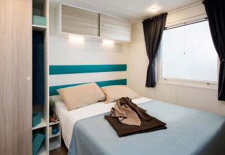 Slaapkamer in Baia Domizia Villaggio Camping I2 stacaravan, tweepersoonsbed en groot raam, modern interieur.