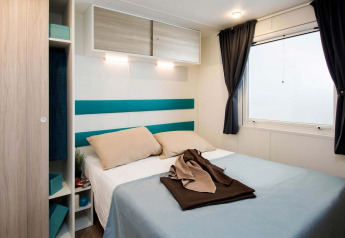 Bedroom inside Baia Domizia Villaggio Camping I2 mobile home, double bed, minimalist decor, large window.