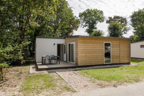 Lodge du Holiday Park Kijkduin 9 avec façade bois, terrasse et meubles d’extérieur au milieu des arbres.