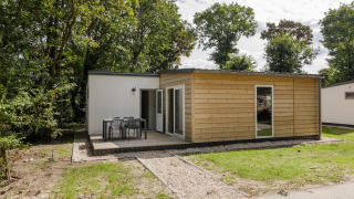Lodge del Holiday Park Kijkduin 9 con fachada de madera, terraza y muebles de exterior entre árboles.