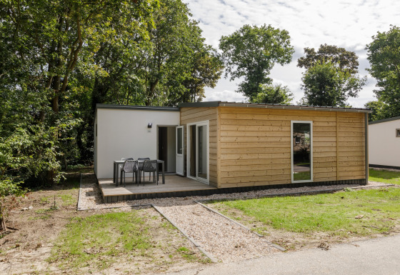 Lodge del Holiday Park Kijkduin 9 con fachada de madera, terraza y muebles de exterior entre árboles.