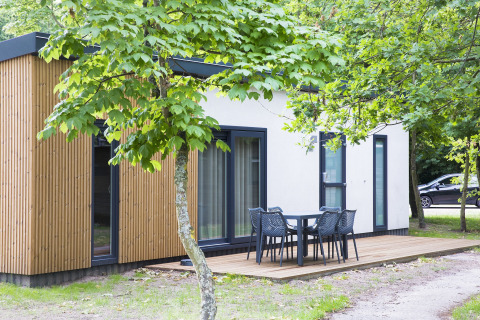 Modern lodge at Holiday Park Kijkduin with a wood panel exterior, deck, and outdoor dining furniture.