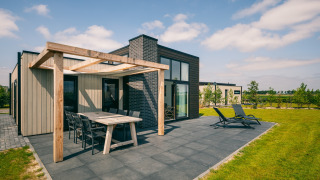 Moderna cabaña en Holiday Park Zeedijk 2 con terraza, muebles de exterior y césped bajo un cielo azul.