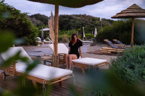 Frau sitzt auf einer Sonnenliege im Holiday Resort Riva degli Etruschi San Vincenzo, Italien, nahe dem Meer.