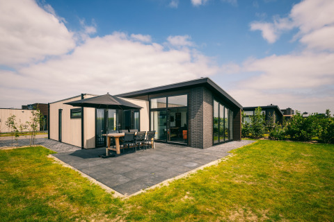 Modern lodge at Holiday Park Zeedijk 3 featuring a patio, outdoor dining set, and large windows on a sunny day.