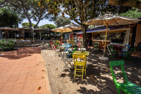 Zona de cafetería exterior en Holiday resort Riva degli Etruschi, San Vincenzo, Italia, con sillas de colores y sombrillas.