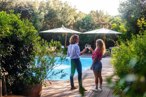 Dos personas brindan con vino junto a la piscina del resort Riva degli Etruschi en Italia, rodeados de árboles.