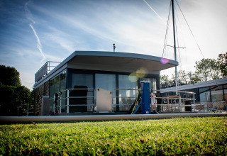 Houseboat moderna chiamata Elysium con terrazza vetrata, ormeggiata su una sponda verde nei Paesi Bassi.