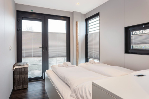 Schlafzimmer im Hausboot Elysium in den Niederlanden mit Doppelbett und modernen Fenstern.