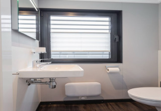 Baño moderno en la casa flotante Elysium en los Países Bajos, con lavabo, ventana y WC.