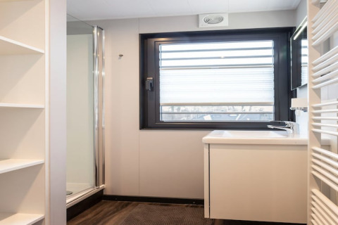 Baño moderno en la casa flotante Elysium en los Países Bajos con ducha, lavabo, ventana y estanterías.