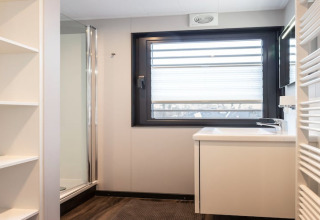 Bagno moderno sulla houseboat Elysium nei Paesi Bassi con doccia, lavandino, scaffali e finestra.