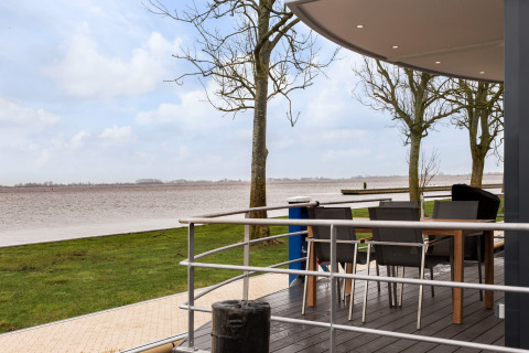 Vista da Houseboat «Elysium» nei Paesi Bassi con terrazza dotata di sedie, tavolo e panorama sul fiume.