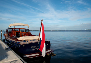 Hausboot 'Elysium' am Steg in den Niederlanden, ruhiges Wasser, Flagge und blauer Himmel sichtbar.