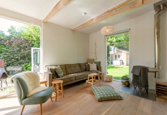 Salon lumineux d’un lodge avec grandes fenêtres, poêle et vue sur jardin à Eureka 109 aux Pays-Bas.