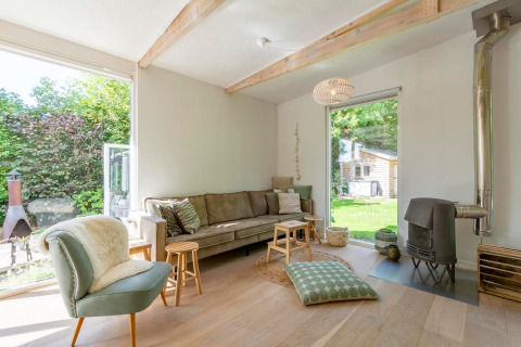 Lyst loungeområde i en lodge med store vinduer, træbjælker og udsigt til en grøn have i Holland.