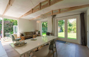 Séjour lumineux et moderne au lodge Eureka 109 aux Pays-Bas, avec grandes fenêtres sur jardin verdoyant.