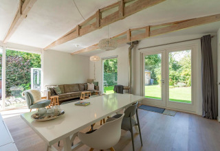 Lyst og moderne opholdsområde i lodge Eureka 109 i Holland med store vinduer ud til en grøn have.