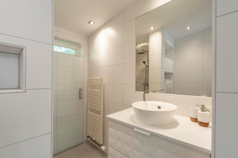 Moderne badeværelse med stor spejl, hvid håndvask, bruseniche og minimalistisk design i Eureka 109.