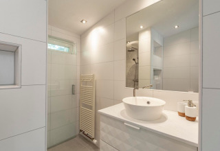 Moderne badeværelse med stor spejl, hvid håndvask, bruseniche og minimalistisk design i Eureka 109.