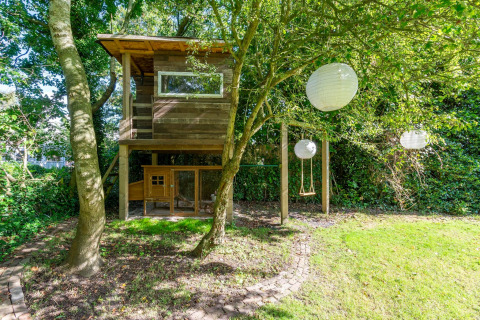 Træhytte med gynge og papirlanterner i grøn have ved lodge Eureka 109 i Holland, omgivet af træer.