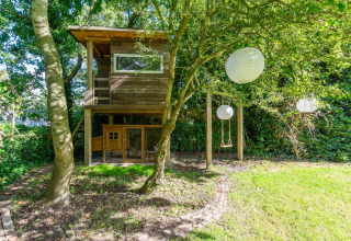 Træhytte med gynge og papirlanterner i grøn have ved lodge Eureka 109 i Holland, omgivet af træer.