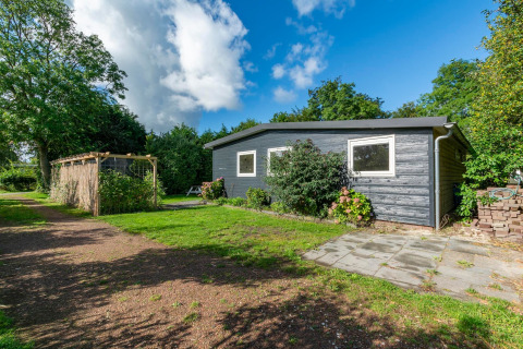 Udendørs billede af lodge 'Eureka 109' i Holland, omgivet af træer, have og en pergola i solskinnet.