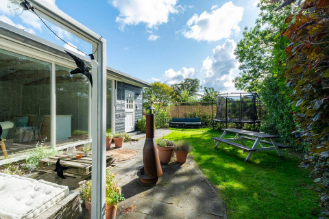 Hyggelig have ved lodge Eureka 109 i Holland med terrasse, bordbænkesæt og trampolin i baggrunden.