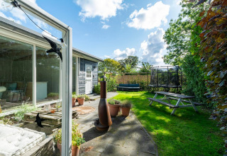 Hyggelig have ved lodge Eureka 109 i Holland med terrasse, bordbænkesæt og trampolin i baggrunden.