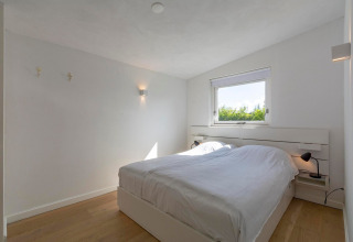 Lyst, minimalistisk soveværelse i Eureka 109-lodgen, Holland, med dobbeltseng og moderne indretning.