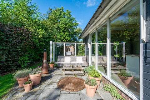 Solrig terrasse ved lodge Eureka 109 i Holland, med havemøbler, blomsterkrukker og grøn udsigt.