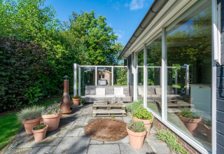 Solrig terrasse ved lodge Eureka 109 i Holland, med havemøbler, blomsterkrukker og grøn udsigt.
